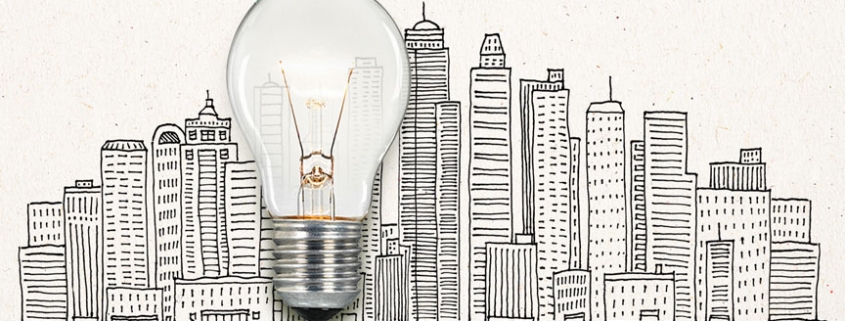Picture of a real illuminated lightbulb laid over an illustrated cityscape