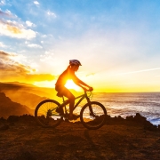 Sunrise silhouette of woman riding her bike on a mountain top