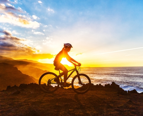 Sunrise silhouette of woman riding her bike on a mountain top