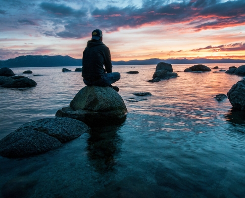 Man sitting alone on a rock in a stream at sunset
