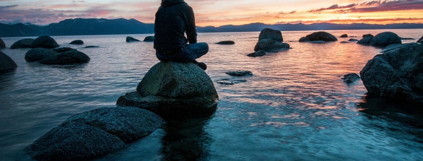 Man sitting alone on a rock in a stream at sunset